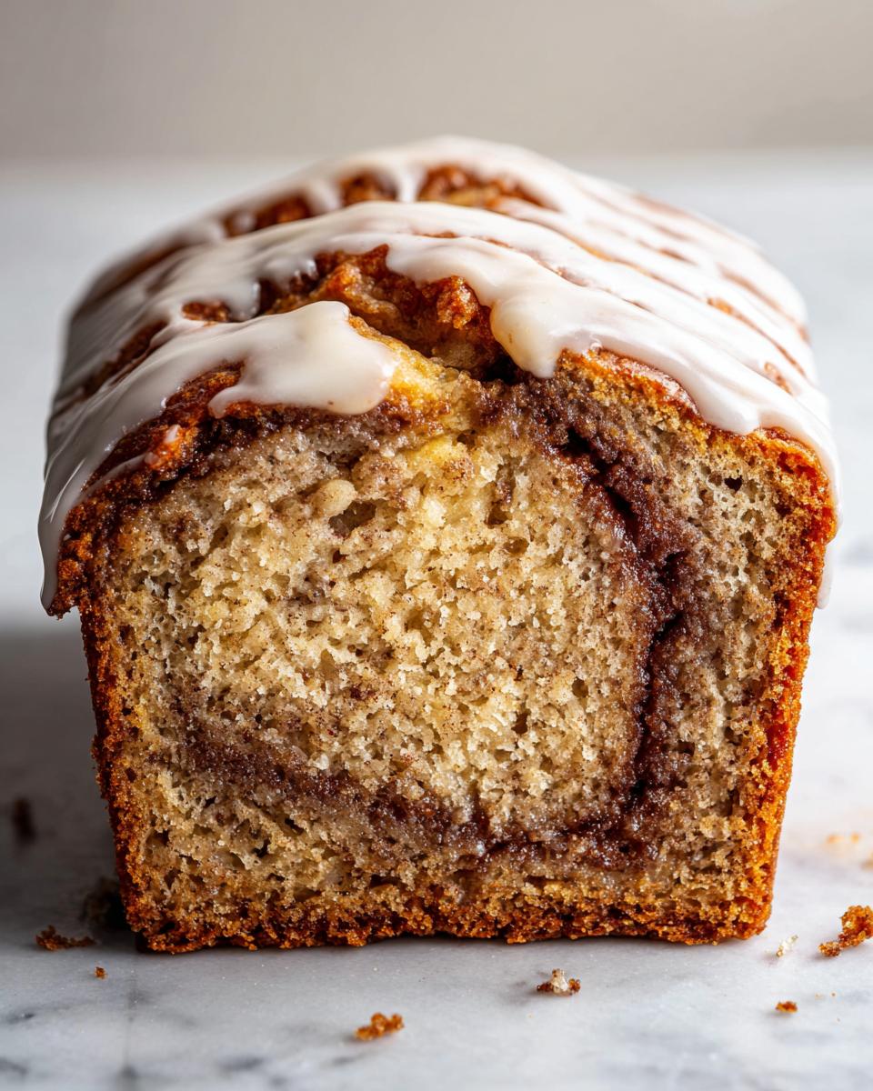 Close-up of a sliced Cinnamon Roll Banana Bread loaf showing the swirl and topped with white icing.