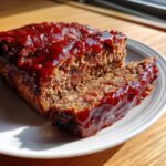 A thick slice cut from a Cracker Barrel Meatloaf, covered in a shiny, dark red glaze.