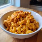 A close-up of creamy BBQ Chicken Mac And Cheese served in a white bowl, topped with paprika.