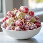 A white bowl filled with red and green grapes coated in a creamy dressing and topped with chopped pecans, showcasing the Creamy Grape Salad.