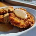 Close-up of crispy Buttermilk Chicken Fried Steak topped with creamy peppered gravy on a white plate.