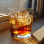 A close-up of a Godfather Cocktail served over ice in a rocks glass, illuminated by bright sunlight.