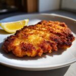 Close-up of perfectly golden, crispy Pork Schnitzel, sliced and served with a lemon wedge.