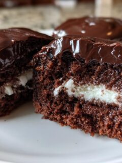 Close-up of Homemade Hostess Cupcakes cut in half showing rich chocolate cake, white cream filling, and glossy chocolate frosting.