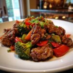 Close-up of glossy Hunan Chicken pieces stir-fried with bright broccoli florets and red bell peppers.