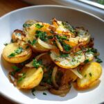 A close-up of golden Lyonnaise Potatoes, sliced and pan-fried with caramelized onions and fresh parsley.