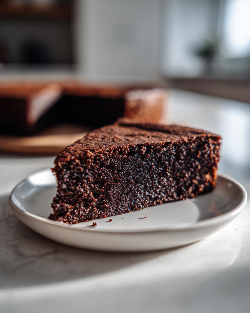 Close-up of a rich, dark slice of moist Gingerbread Cake resting on a small white plate.
