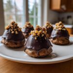 Five delicious no-bake Oreo Acorns dipped in chocolate and topped with chopped nuts, resting on a white plate.