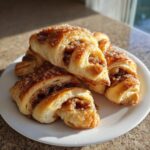 A stack of golden brown Pecan Pie Crescent Rolls, glistening with sugar topping, served on a white plate.