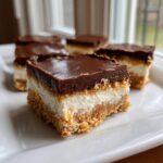 A close-up of a rich Chocolate Cheesecake Bars square showing the graham cracker crust, creamy filling, and thick chocolate topping.