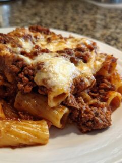 A close-up serving of baked Rigatoni Al Forno topped with rich meat sauce and melted mozzarella cheese.