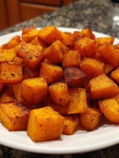 A white plate piled high with perfectly roasted, seasoned cubes of butternut squash.