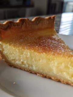 A close-up slice of creamy Salted Honey Pie with a golden brown, crimped crust, dusted with powdered sugar.