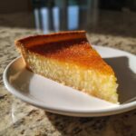 A close-up slice of Amazing Salted Honey Pie with a rich, golden-brown caramelized top, served on a white plate.