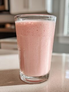 A tall glass filled with a frothy, light pink Smoothie King Angel Food Smoothie.