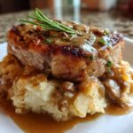 A thick, seared pork chop smothered in mushroom gravy served atop mashed potatoes, part of a Smothered Pork Chop and Scalloped Potato Casserole.