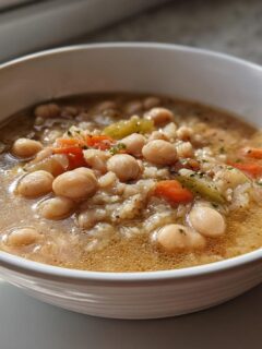 Close-up of a white bowl filled with White Chickpea Chili, featuring chickpeas, rice, carrots, and celery in a savory broth.