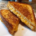 Two halves of a golden brown Air Fryer Grilled Cheese sandwich with melted, gooey cheddar cheese oozing out.