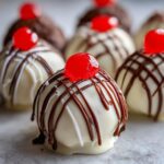 Close-up of a white chocolate Banana Split Truffles topped with a maraschino cherry and drizzled with dark chocolate.