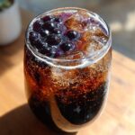 Close-up of a fizzy, dark soda drink topped with purple Bat Wing Bubble Tea boba pearls and ice cubes.
