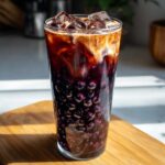 Close-up of a tall glass of Bat Wing Bubble Tea layered with dark purple boba pearls, coffee, and cream.