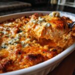 A spoonful of creamy, cheesy Buffalo Bat Nest Dip topped with blue cheese crumbles being lifted from a white baking dish.