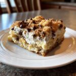 A square slice of rich Cannoli Squares featuring layers of cake, cream filling, and a crumble topping with mini chocolate chips.