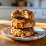 Three stacked Caramel Apple Cookies heavily drizzled with thick, glossy caramel sauce on a small plate.