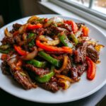 A close-up of glistening Chinese Pepper Steak With Onions featuring tender beef strips, green bell peppers, red peppers, and caramelized onions.