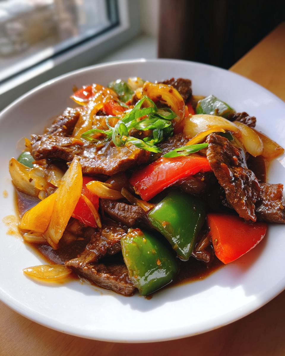 Close-up of Chinese Pepper Steak With Onions, featuring beef slices, green, red, and yellow peppers, and onions in a dark sauce.