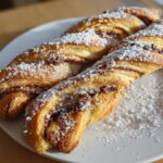 Two golden-brown Chocolate Chip Cookie Dough Twists dusted heavily with coarse sugar on a white plate.
