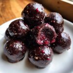 A stack of rich, dark Chocolate Covered Cranberry Sauce bites on a white plate, showing a gooey cranberry filling inside one.