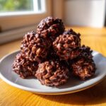 A stack of glossy Chocolate Rice Krispie Balls coated in rich melted chocolate, served on a light grey plate.