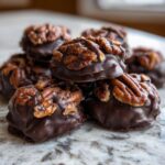 A close-up stack of rich, dark chocolate Christmas Pecan Turtles topped with candied pecans.