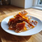 A pile of broken, amber-colored pieces of Classic Christmas Toffee stacked on a white plate.
