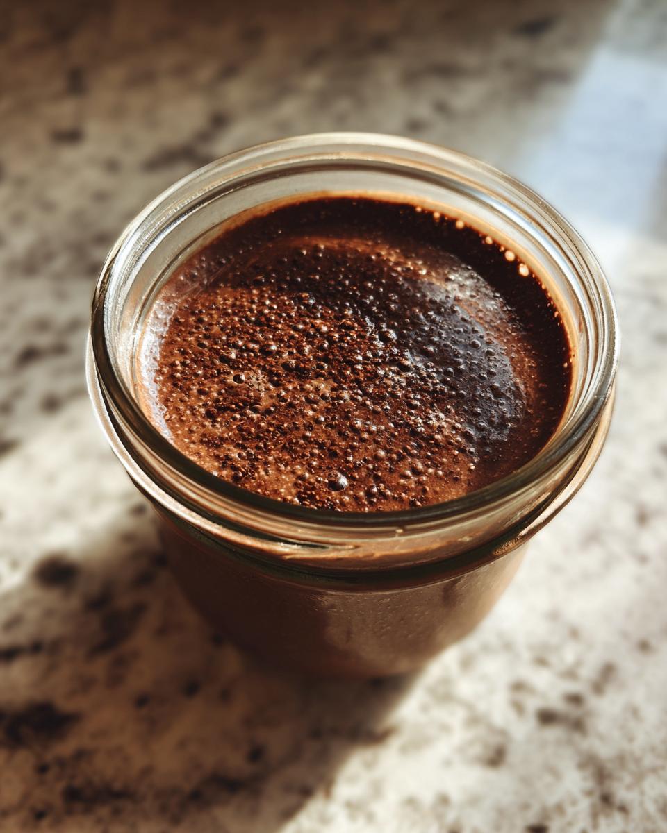 Overhead close-up of rich, creamy chocolate protein overnight oats in a glass jar with a bubbly top layer.