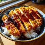Close-up of sliced, crispy panko-crusted pork served over white rice in a bowl, drizzled with dark sauce for Japanese Katsu Bowls.