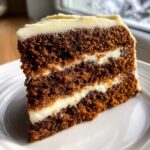 Close-up of a moist slice of Gingerbread Layer Cake showing two dark brown layers separated by thick white cream cheese frosting.