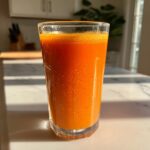 A tall glass filled with vibrant, freshly made Pumpkin Juice sitting on a sunlit marble counter.