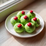 A plate of six bright green Grinch Oreo Balls, each topped with a single red M&M candy.