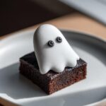 A rich, dark chocolate brownie topped with a white, shimmering fondant ghost decoration for Halloween Ghost Brownies.
