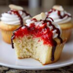 Close-up of a Halloween Vampire Bite Cupcake with a bite taken out, showing the red filling, white frosting, and chocolate drizzle.