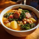 Close-up of a bowl of Hearty Sausage Soup With Potatoes Beans And Kale, showing broth, sausage slices, potatoes, and kale.