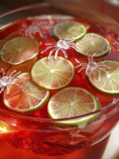 Close-up of Hocus Pocus Halloween Punch in a glass bowl, garnished with lime slices and plastic spiders.