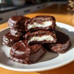 A stack of homemade chocolate covered Peppermint Patties, with two cut in half showing the white mint filling.