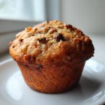 A single, large, golden-brown Monster Muffin topped with chopped nuts, sitting on a white plate.