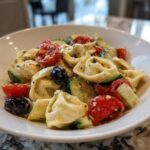 A close-up view of a creamy Italian Tortellini Pasta Salad featuring tortellini, cucumber chunks, halved cherry tomatoes, and black olives.