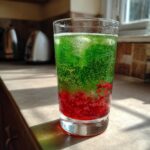 A tall glass filled with a bubbly, layered Zombie Punch Mocktail, featuring bright green liquid over a dense red layer.