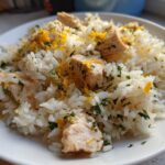 Close-up of a white plate piled high with Lemon Herb Chicken And Rice, garnished with fresh parsley and bright yellow lemon zest.