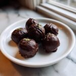 Six dark chocolate-coated Mint Oreo Truffles, drizzled with chocolate and topped with green sprinkles, resting on a white plate.